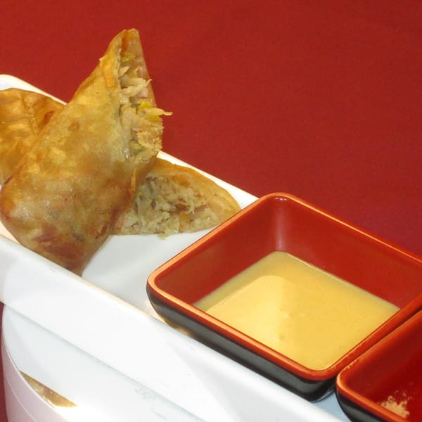 Crispy Thai spring rolls with a savory filling, served with two dipping sauces on a white plate.