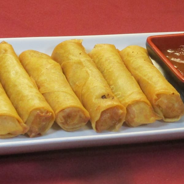 Golden-brown Thai spring rolls arranged on a white rectangular plate with a side of dipping sauce.