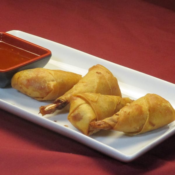 Golden-fried Thai shrimp spring rolls with a sweet chili dipping sauce on a white rectangular plate.