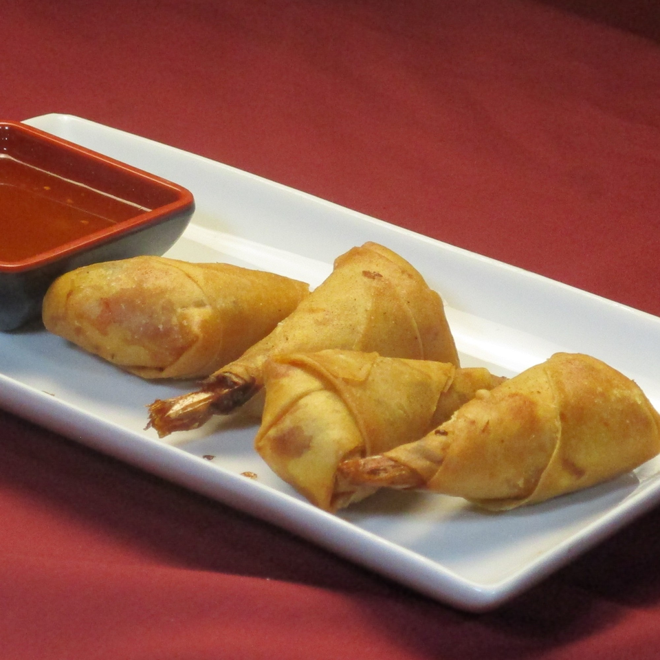 Golden-fried Thai shrimp spring rolls with a sweet chili dipping sauce on a white rectangular plate.
