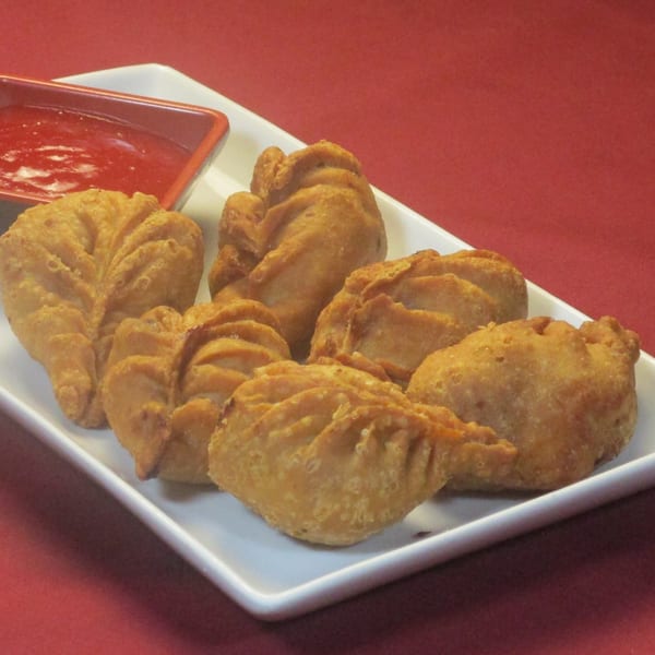 Golden-brown Thai curry puffs with crimped edges, served with a side of red dipping sauce.
